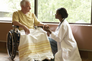 Doctor comforting patient in wheelchair by windows in hospital