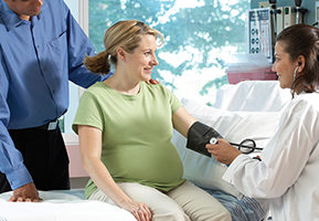 Side profile of a female doctor checking the blood pressure of a pregnant woman