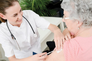 cheerful young nurse giving vaccine injection to elderly woman home